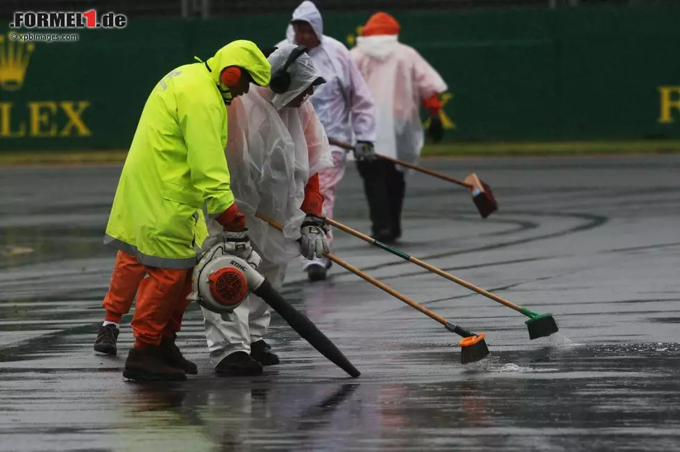 Foto zur News: Mit vollem Einsatz versuchten die Streckenposten, den Kurs einigermaßen von Pfützen zu befreien