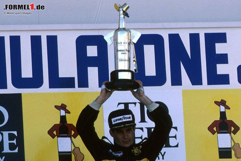 Foto zur News: Jerez 1986: Ayrton Senna reckt den besonderen Siegerpokal, der die Form einer Sherry-Flasche hat. Für das Getränk ist Jerez de la Frontera berühmt - und nutzt den Grand Prix als Werbemaßnahme. Sponsor Tio Pepe setzt dem Flaschen-Pokal einen Hut auf und stellt sogar eine Miniatur-Gitarre dazu!